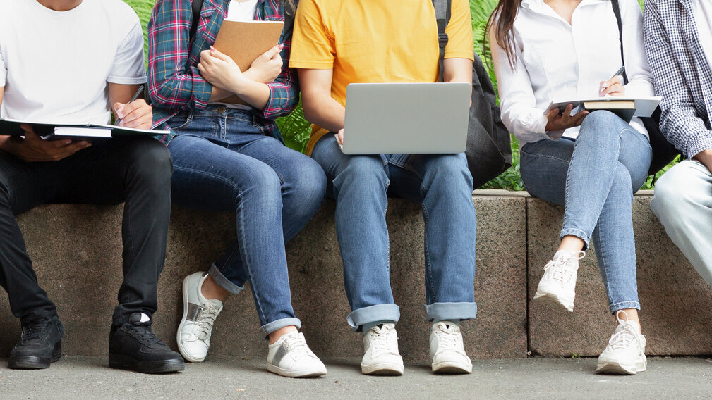 Jugendliche sitzen auf einer Steinmauer und blicken in einen Laptop