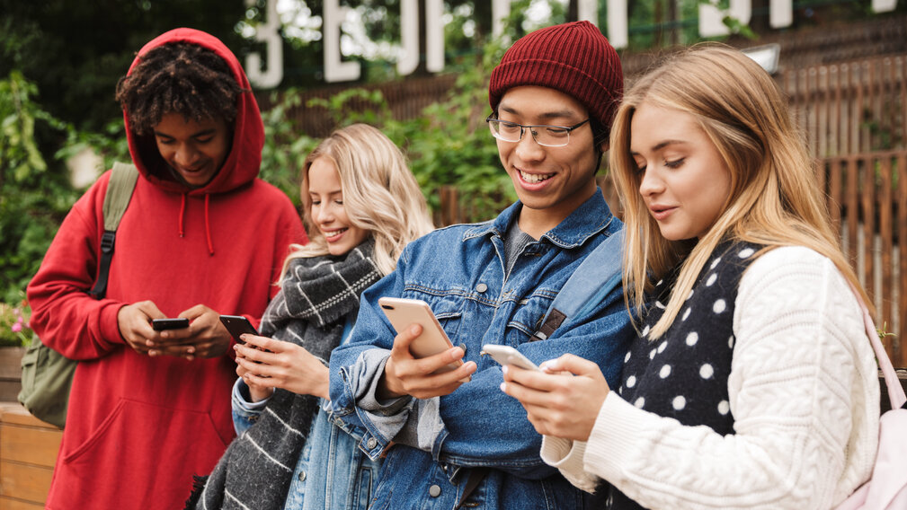 Vier Jugendliche stehen nebeneinander und blicken in ihre Smartphones