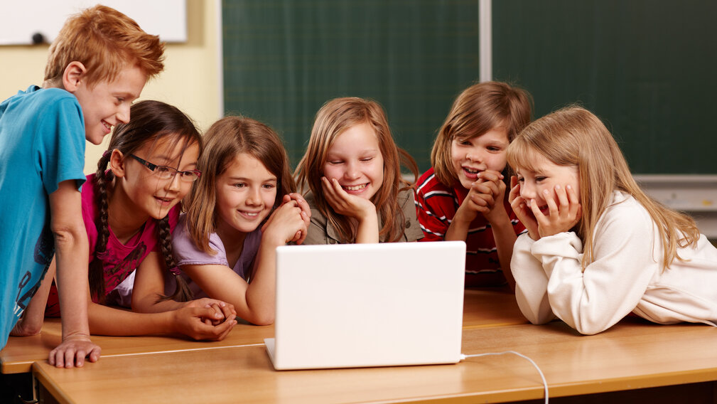 Lachende Kinder blicken zusammen in einen Laptop